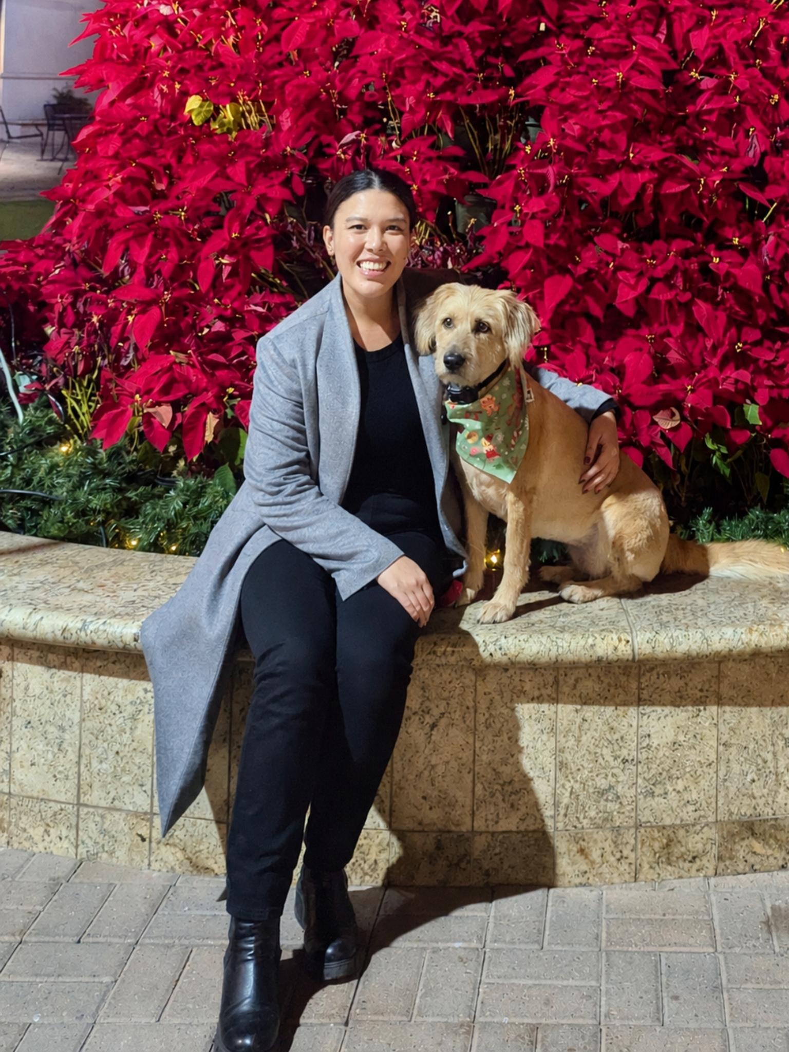 Jacinda Stephens sits with her dog Millie in front of a large vibrant red bush.